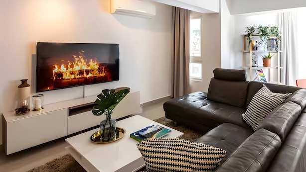 A modern living room with a flat-screen TV, a leather sofa, a coffee table, and a bookshelf. - 2br Kingbed Kids Play Area No Surgery (Santo Domingo)