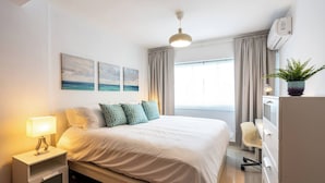 A hotel room with a bed, bedside table, lamp, curtains, a potted plant, and artwork on the wall. - 2br Kingbed Kids Play Area No Surgery (Santo Domingo)