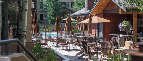 Un espace extérieur aménagé en terrasse, avec des tables, des chaises, des parasols et une piscine.