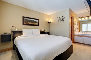 A neatly arranged bedroom with a large bed, a bedside table with a lamp, a painting on the wall, and a bathroom with a mirror and sink. - TR1208 | Quiet Location in Building | Winter Shuttle | 10 Hot Tubs (Steamboat Springs)