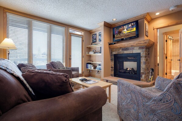 A cozy living room with a fireplace, comfortable seating, and a television mounted above it. - TR1208 | Quiet Location in Building | Winter Shuttle | 10 Hot Tubs (Steamboat Springs)