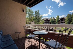A covered outdoor seating area with a table and chairs, overlooking a building with multiple windows and a clear sky. - TR1208 | Quiet Location in Building | Winter Shuttle | 10 Hot Tubs (Steamboat Springs)