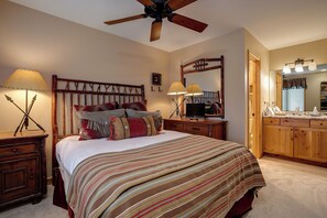 Ein Schlafzimmer mit einem Holz-Kopfteil, einem Bett mit gestreifter Bettwäsche, zwei Nachttischlampen, einem Deckenventilator, einem Spiegel und einem Holzschrank.