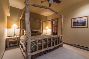 Ein Bett mit Baldachin im rustikalen Stil, zwei Nachttische mit Lampen, ein Deckenventilator und ein gerahmtes Bild an der Wand.