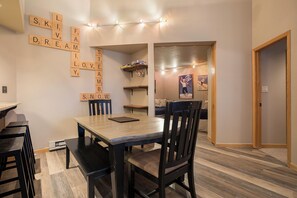A dining area with a wooden table, chairs, and a wall with Scrabble tiles spelling out words. - TR1302 | Nicely Updated Condo | Ski Lockers | A/C | 10 Hot Tubs (Steamboat Springs)