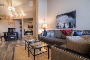A living room with a sofa, a coffee table, a dining table with chairs, a lamp, and a wall with a framed picture. - TR1302 | Nicely Updated Condo | Ski Lockers | A/C | 10 Hot Tubs (Steamboat Springs)