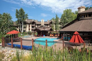 A pool area with a wooden fence, lounge chairs, and umbrellas. - TR1302 | Nicely Updated Condo | Ski Lockers | A/C | 10 Hot Tubs (Steamboat Springs)