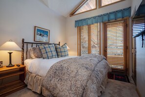Un dormitorio con cama, mesita de noche, lámpara, un cuadro en la pared y una ventana con persianas.