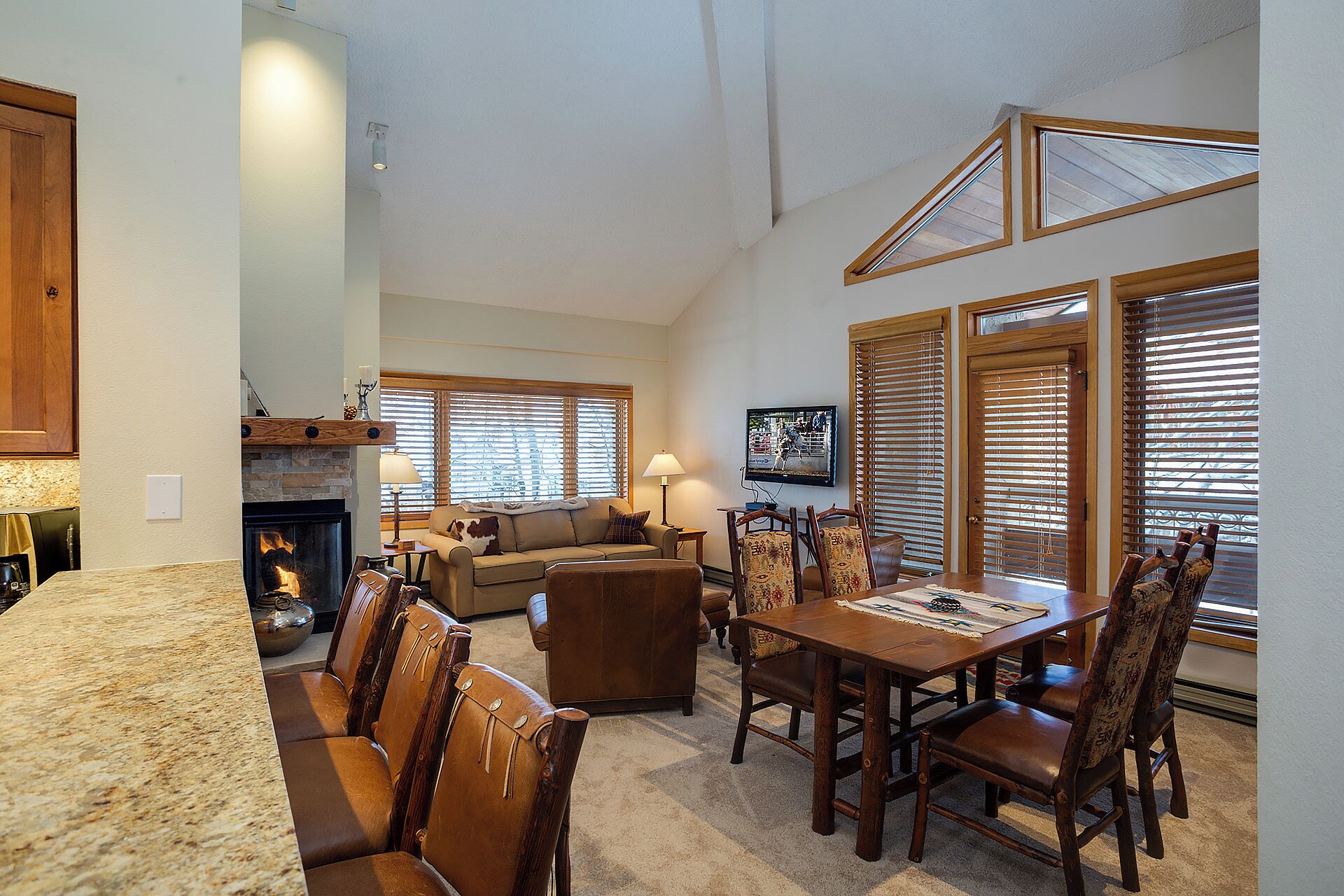 A spacious living area with a fireplace, a dining table with chairs, a sofa, and a television mounted on the wall.