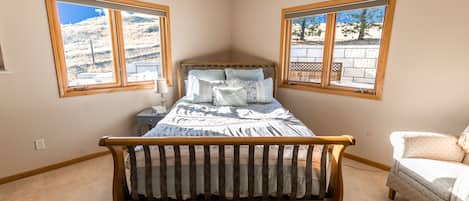Quarto com cama de madeira, duas janelas com vista, mesa de cabeceira e uma cadeira.