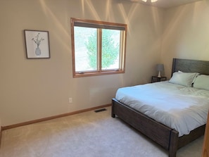 A bedroom with a bed, a nightstand, a lamp, a window, and a framed picture on the wall.