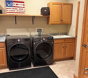 A laundry room with two front-loading washing machines, wooden cabinets, a sink, and a sign above the machines.