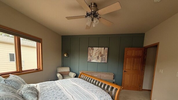 Quarto com cama, ventoinha no teto, janela, porta e quadro na parede.