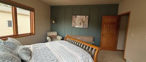 A bedroom with a bed, a ceiling fan, a window, a door, and a wall-mounted picture.