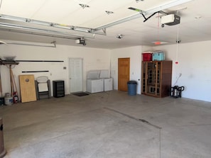 A garage with a concrete floor, a white door, a wooden cabinet, and various tools and equipment.