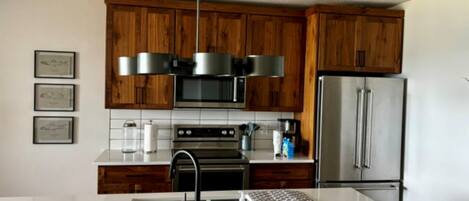 A modern kitchen with wooden cabinets, stainless steel appliances, and a white countertop.