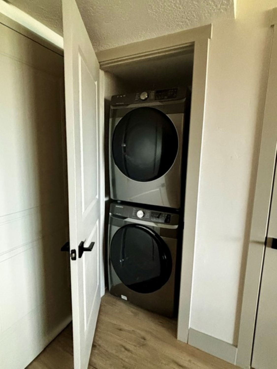 A laundry room with two stacked washing machines and a door leading to another room.