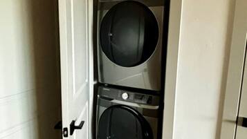 A laundry room with two stacked washing machines and a door leading to another room.