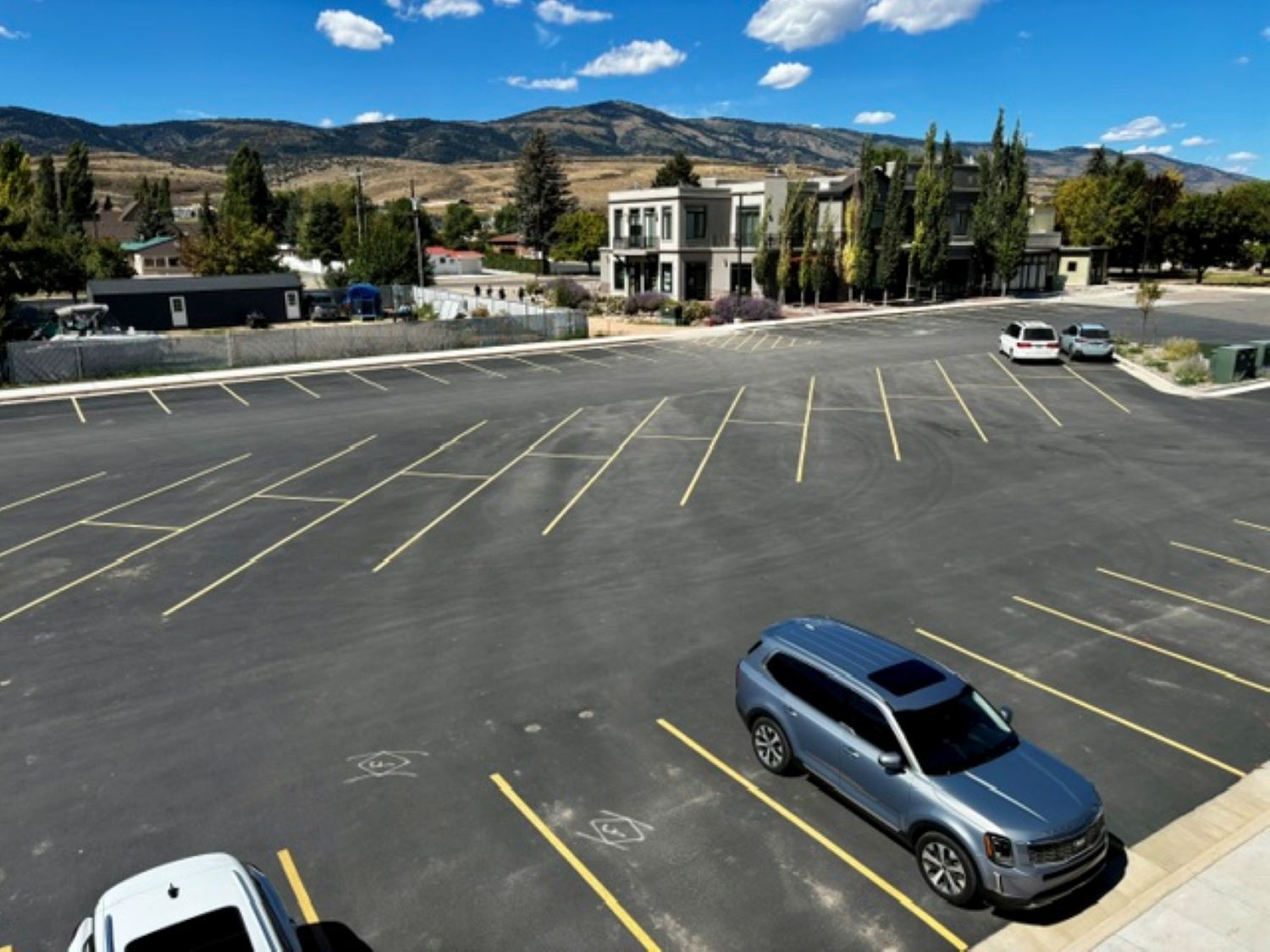 A parking lot with multiple parking spaces, a few cars, and a building with a modern design in the background.