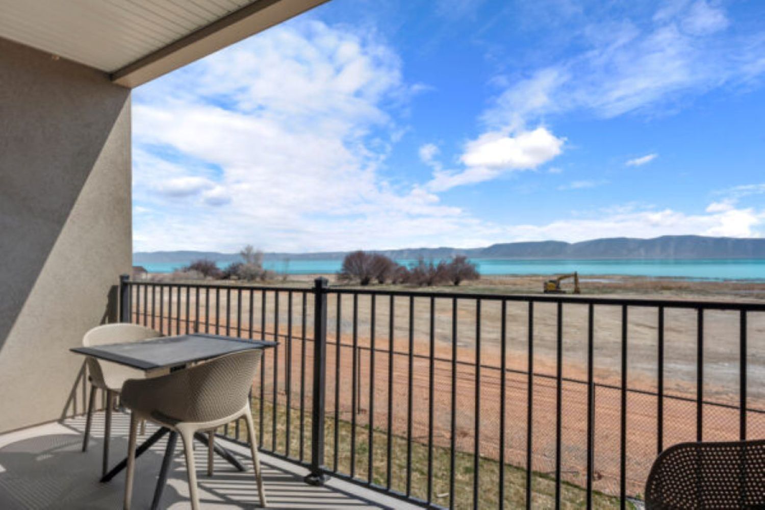 A balcony with a table and chairs, a view of a beach, and a clear sky.