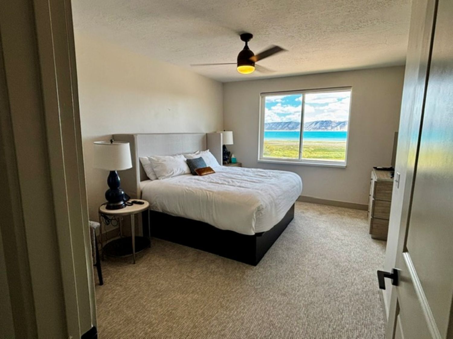 A bedroom with a bed, two bedside tables, a ceiling fan, and a window with a view of the outdoors.