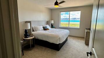 A bedroom with a bed, two bedside tables, a ceiling fan, and a window with a view of the outdoors.