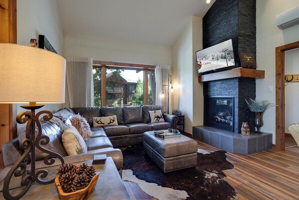 A cozy living room with a sectional sofa, a fireplace, and a large window overlooking a scenic view. - TR1304 | Perfect Mountain Getaway | Modern Décor | A/C | Hot Tubs (Steamboat Springs)