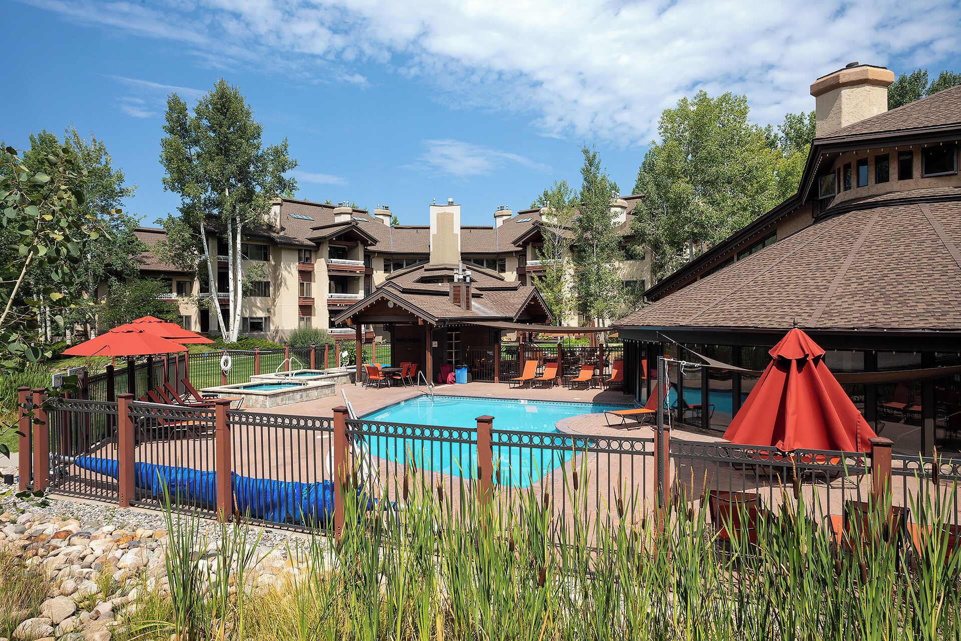 A pool area with a wooden fence, lounge chairs, and umbrellas.