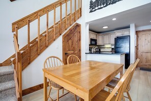 A wooden staircase leading to a kitchen area with white cabinets, a black refrigerator, and a dining table with chairs. - TR1307 | Recently Updated | Gorgeous and Unique Space | A/C | Hot Tub (Steamboat Springs)