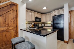 A kitchen with wooden cabinets, a black refrigerator, a microwave, and a granite countertop. - TR1307 | Recently Updated | Gorgeous and Unique Space | A/C | Hot Tub (Steamboat Springs)