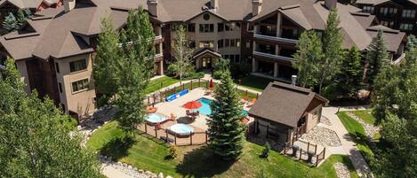 Aerial view of the property nestled in a tree-lined neighborhood, showcasing the central pool area and surrounding residential community.