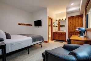 A hotel room with a bed, a desk, a chair, a bathroom with a sink and mirror, and wooden cabinets. - TR1307 | Recently Updated | Gorgeous and Unique Space | A/C | Hot Tub (Steamboat Springs)