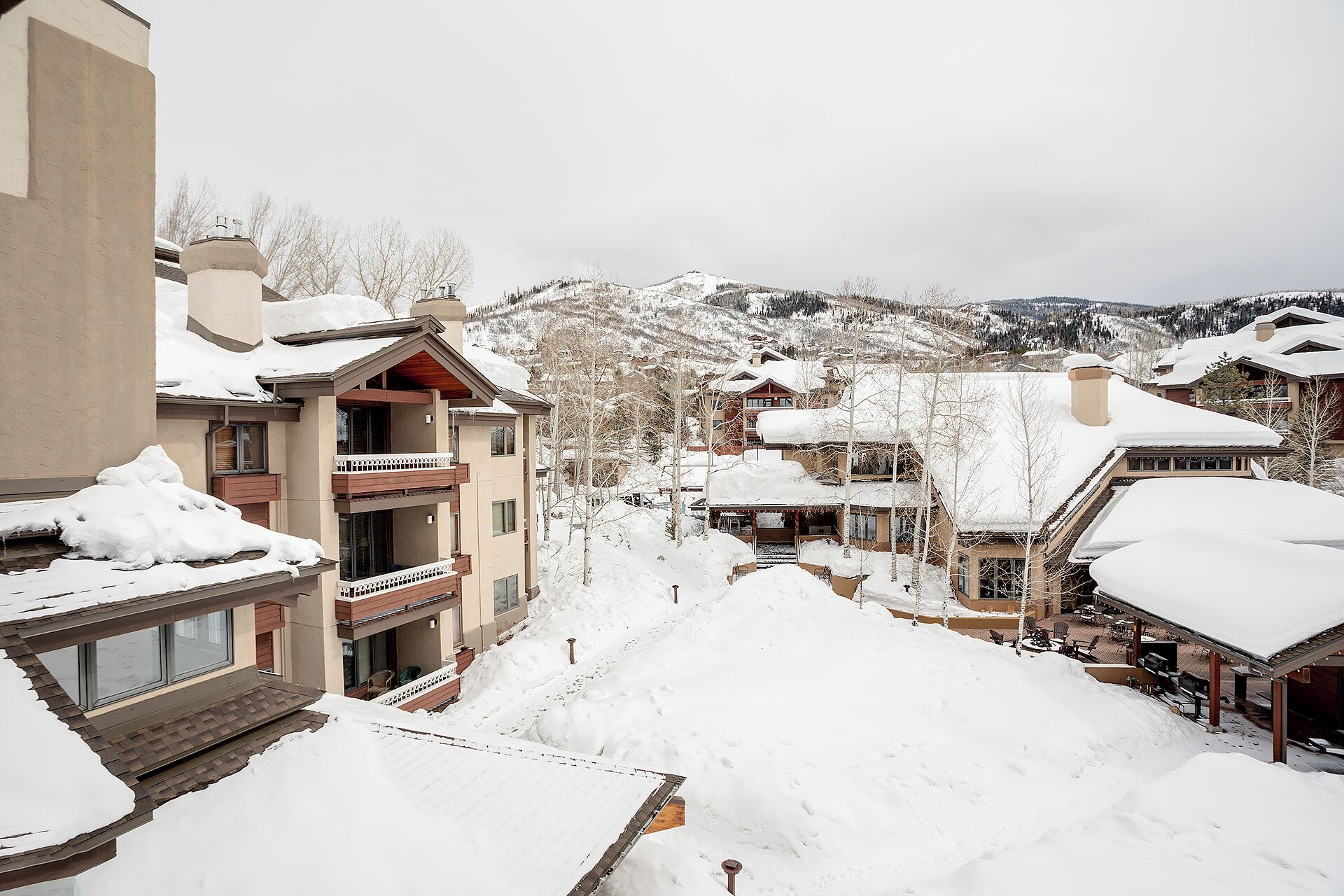 A snow-covered mountain town with multi-story buildings, balconies, and a ski slope in the background.