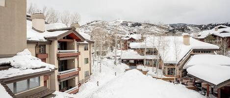 Un pueblo cubierto de nieve con edificios de varios pisos, balcones y una pista de esquí al fondo.
