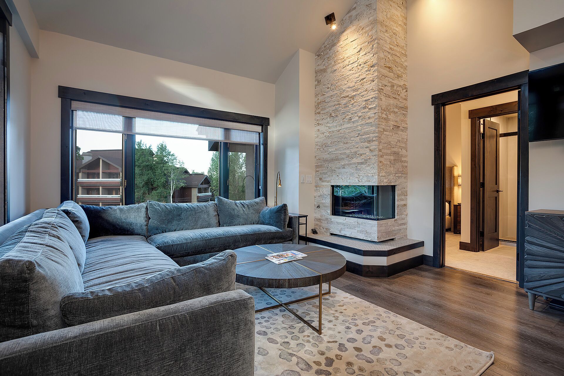A modern living room with a sectional sofa, a round coffee table, and a stone fireplace.