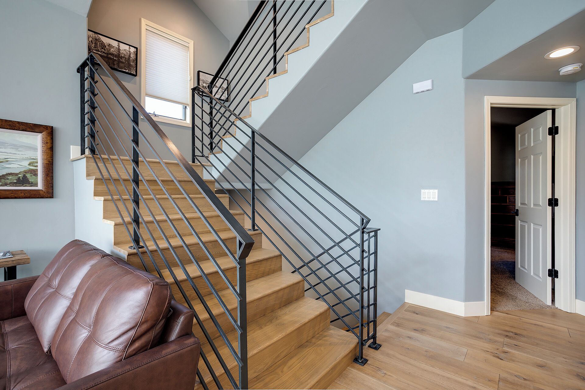 A staircase with wooden steps and black metal railings, a brown leather chair, and a door leading to another room.