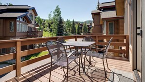 Una terraza de madera con sillas y una mesa de metal, con vistas a un área boscosa.