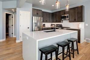 A modern kitchen with a large island, stainless steel appliances, dark wooden cabinets, and pendant lighting. - ER5 | A/C | New Listing | Gorgeous Townhome on the Mtn | Hot Tub (Steamboat Springs)