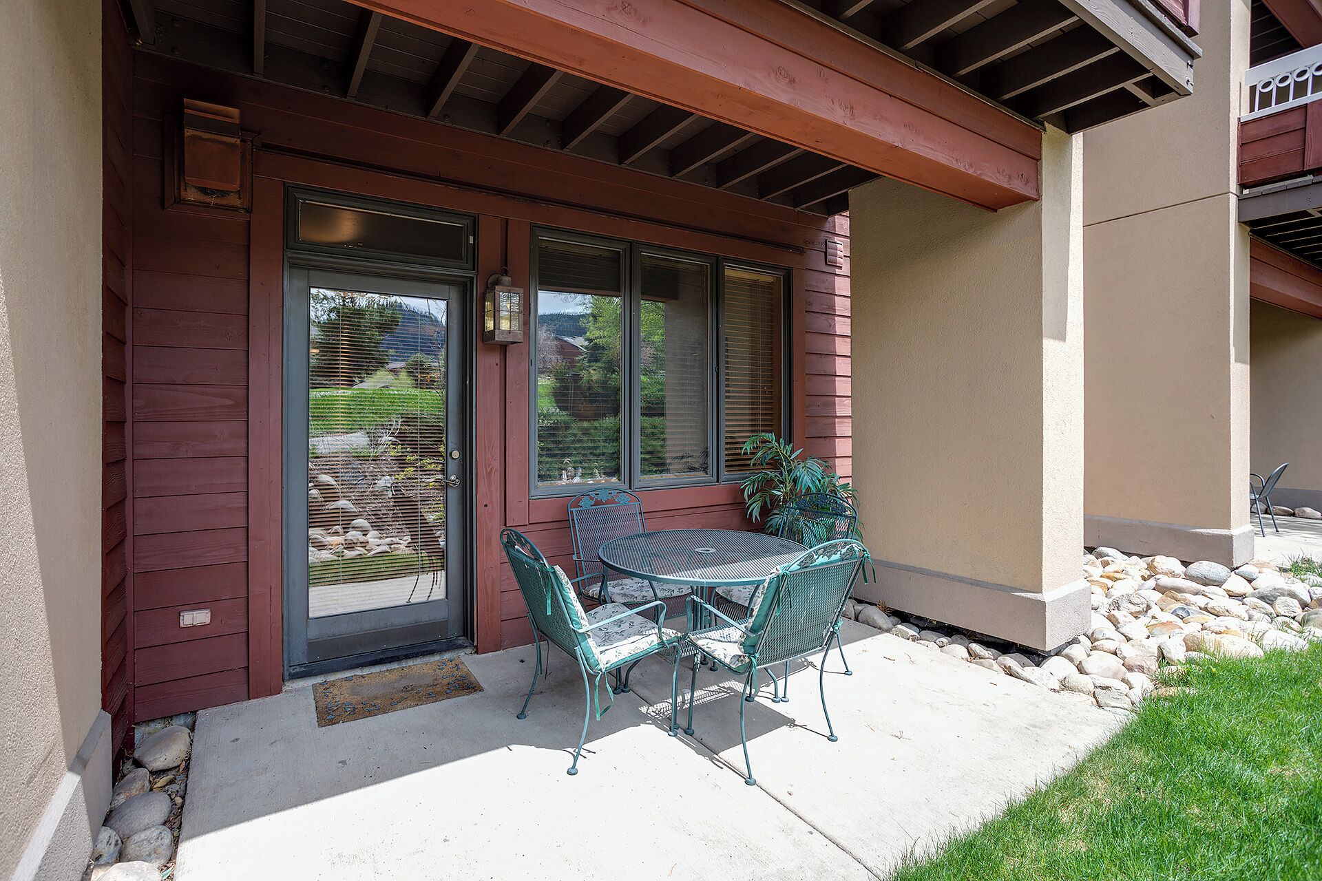 A covered patio with a table and chairs, a door, and a window with blinds.