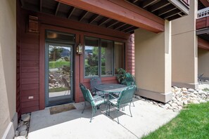 A covered patio with a table and chairs, a door, and a window with blinds. - TL2104 | Short Walk to Skiing | 10 Hot Tubs | Winter Shuttle | 4 Pools (Steamboat Springs)
