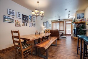 Een eetgedeelte met een houten tafel en stoelen, een kroonluchter en lijstjes met afbeeldingen aan de muur.