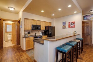 A kitchen with wooden cabinets, a microwave, a refrigerator, a sink, and a bar area with stools. - TL2104 | Short Walk to Skiing | 10 Hot Tubs | Winter Shuttle | 4 Pools (Steamboat Springs)