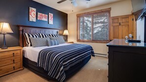 Un dormitorio con cama, mesitas de noche, cómoda, ventilador de techo y ventana con persianas.