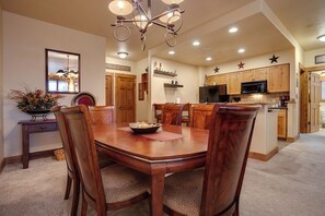 A dining area with a wooden table and chairs, a chandelier, and a kitchen in the background. - TL2203 | Cozy Condo | Nice View | Short Walk to Slopes | Winter Shuttle (Steamboat Springs)