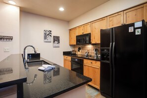 A kitchen with a black refrigerator, wooden cabinets, a black countertop, a stainless steel sink, and a microwave. - TL2209 | Close to Slopes | A/C | 10 Hot Tubs | 4 Pools (Steamboat Springs)