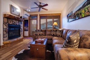 A cozy living room with a stone fireplace, leather sofa, and a large painting. - TL2209 | Close to Slopes | A/C | 10 Hot Tubs | 4 Pools (Steamboat Springs)