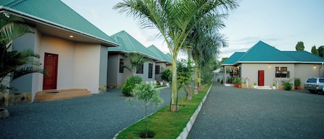 A row of single-story houses with green roofs, a central grassy area, and a gravel driveway.