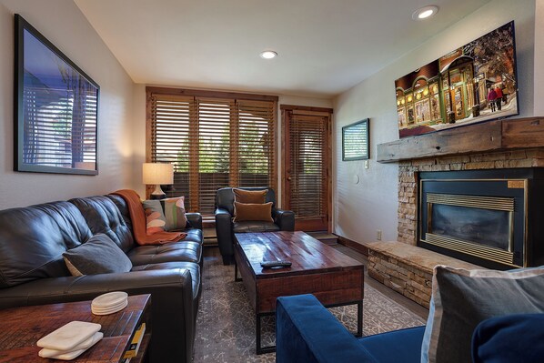 A living room with a fireplace, leather sofa, wooden coffee table, and a painting above the fireplace. - TR1102 | Mountain Getaway | 10 Hot Tubs | 4 Pools | Winter Shuttle (Steamboat Springs)