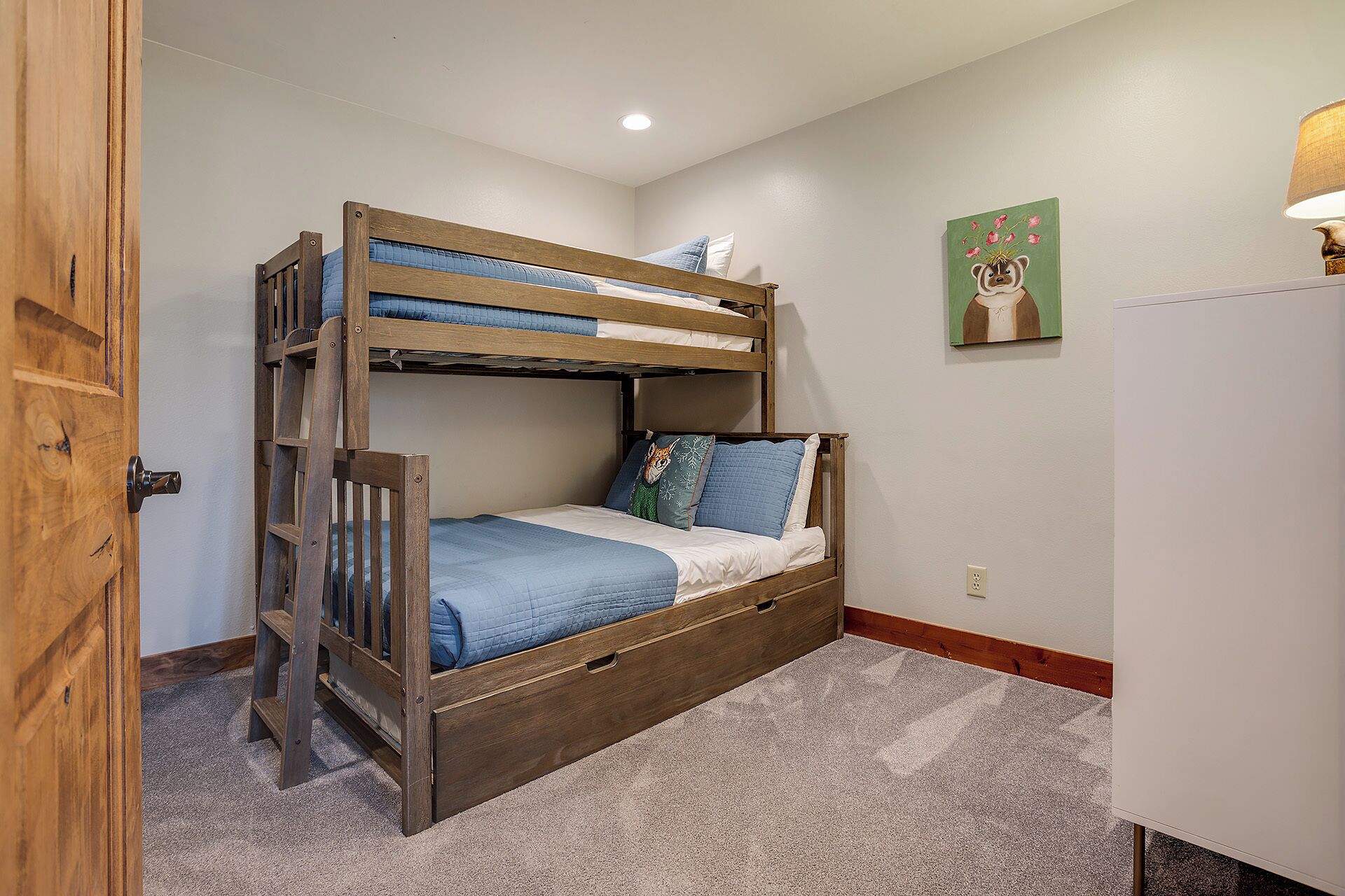 Un letto a castello con struttura in legno, un giroletto blu sul letto inferiore e un materasso bianco sopra.