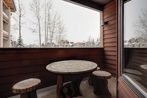 Ein Eckbalkon mit rundem Tisch und zwei hölzernen Hocker, mit Blick auf eine verschneite Wohngegend.